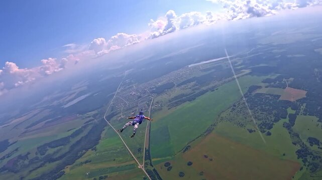 A skydiver performs a backfly element while free-falling over fields and clouds. Extreme sports, adrenaline, altitude and aviation.
