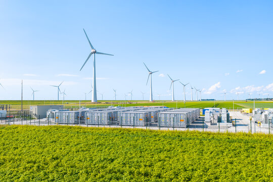 Aerial view of battery energy storage system facility next to wind turbines. Industrial lithium battery system for renewable power plant and grid management.