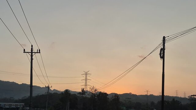 Silhouette of power lines and utility poles against a beautiful sunset sky with mountains in the background.