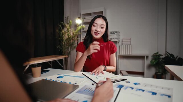 Two young Asian businesswomen discussing financial data and company growth strategy. The team leader is brainstorming creative ideas at night