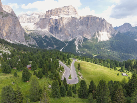 Aerial view of Sella Pass winding through the lush green alpine meadows and dense pine forests of the Dolomites in Selva, Trentino-Alto Adige, Italy.