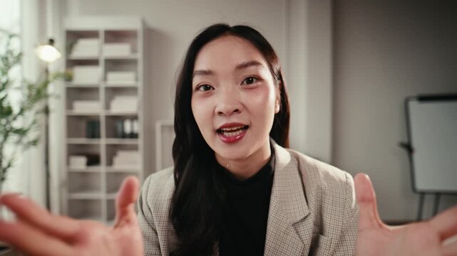 POV of an attractive young asian businesswoman looking at the camera and talking on an online conference call from her modern office
