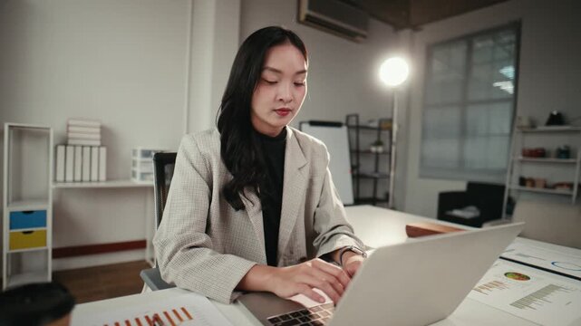 Serious asian businesswoman working on a laptop computer in a modern office. Ambitious female entrepreneur thinking and typing on her keyboard