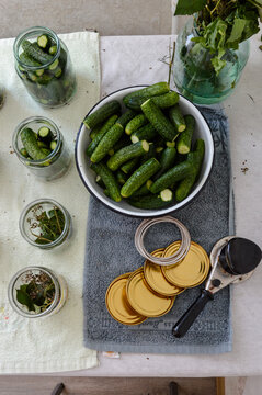 Top view of home canning workspace with cucumbers in bowl, glass jars, metal lids and seamer tool. Autumn harvesting, vegetable pickling, food preservation and DIY prep concept