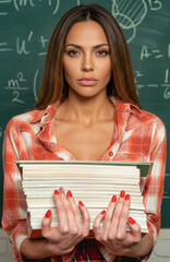 Fototapeta premium Young female teacher or student holding stack of books in front of green chalkboard.