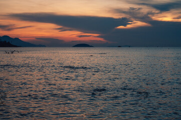 Fototapeta premium Crowds of people enjoying a warm morning swim in the ocean during a colorful sunset, creating a relaxing summer beach atmosphere, Nha Trang, Vietnam