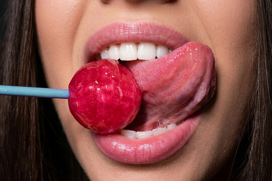 Extreme macro shot of woman licking bright red lollipop showing mouth, lips, and teeth.