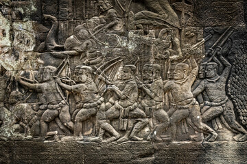 Fototapeta premium Ancient sandstone bas-relief depicting a historical battle and warriors on the walls of Bayon Temple in Angkor Thom, Siem Reap, Cambodia