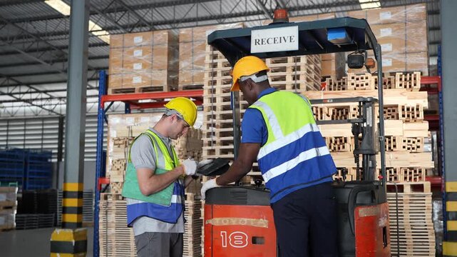 Workers check a device while standing near a forklift in a warehouse setting during daylight hours