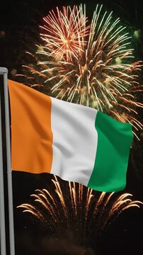 The national flag of Ivory Coast waving majestically against a festive fireworks display at night.