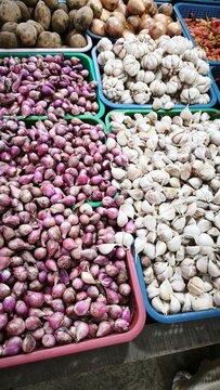 View of a vibrant market stall displaying baskets of fresh ginger, red chilies, garlic, limes, and onions