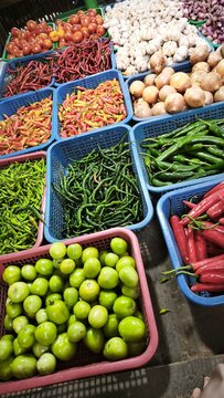 View of a vibrant market stall displaying baskets of fresh ginger, red chilies, garlic, limes, and onions