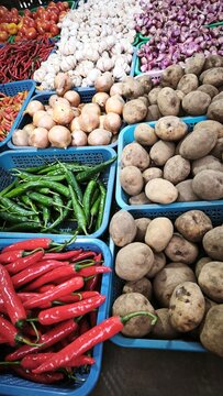 View of a vibrant market stall displaying baskets of fresh ginger, red chilies, garlic, limes, and onions