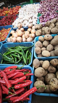 View of a vibrant market stall displaying baskets of fresh ginger, red chilies, garlic, limes, and onions