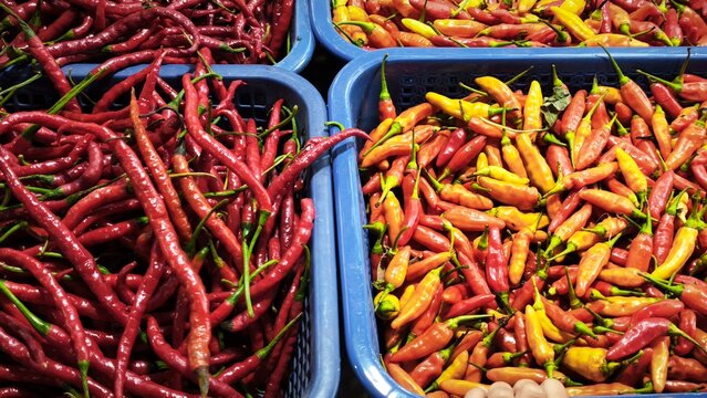 View of a vibrant market stall displaying baskets of fresh ginger, red chilies, garlic, limes, and onions