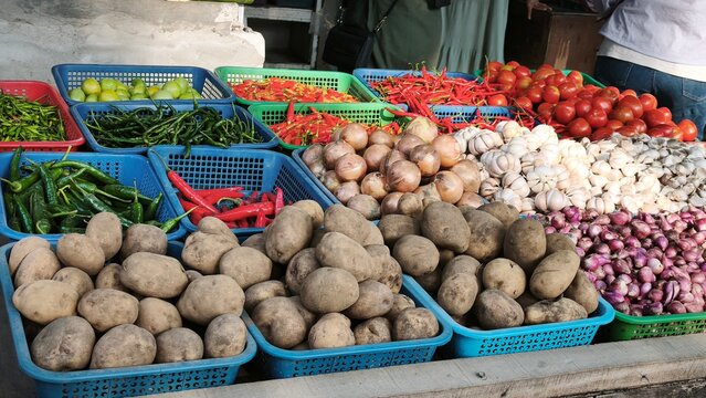 View of a vibrant market stall displaying baskets of fresh ginger, red chilies, garlic, limes, and onions