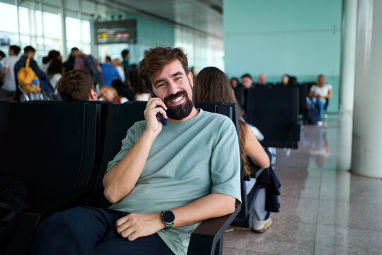 Smiling man sitting and enjoying a phone conversation while waiting for his flight at the airport departure area.
