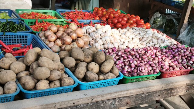 View of a vibrant market stall displaying baskets of fresh ginger, red chilies, garlic, limes, and onions