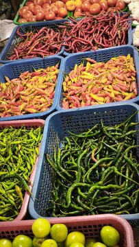 View of a vibrant market stall displaying baskets of fresh ginger, red chilies, garlic, limes, and onions