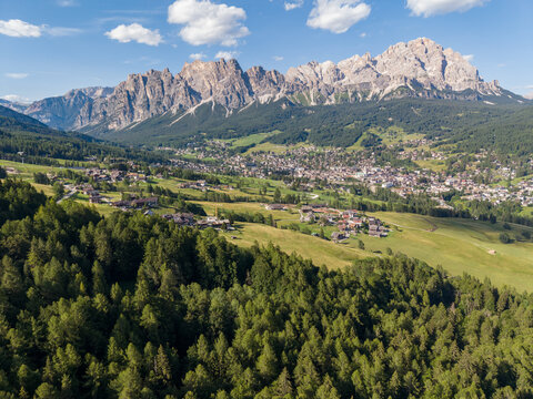 Aerial view of the alpine town of Cortina d'Ampezzo nestled in the Dolomites with Tofane mountains and lush green forests in the foreground, Cortina d'Ampezzo, Veneto, Italy.