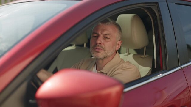 Mature Caucasian driver looking at side mirror while maneuvering red car, 4K