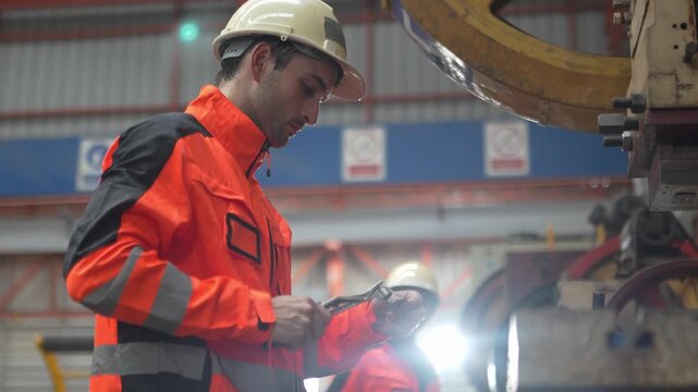 Workers in safety gear operate machines in a factory setting during the day