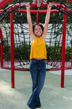 Teen girl smiling, happily hanging on playground structure