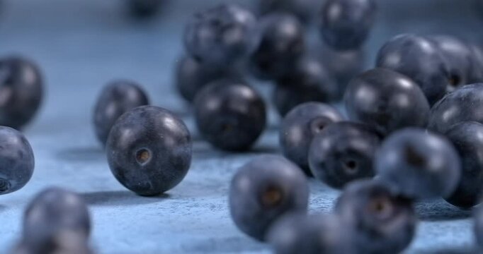 Fresh blueberries fall and bounce across a blue surface in slow motion