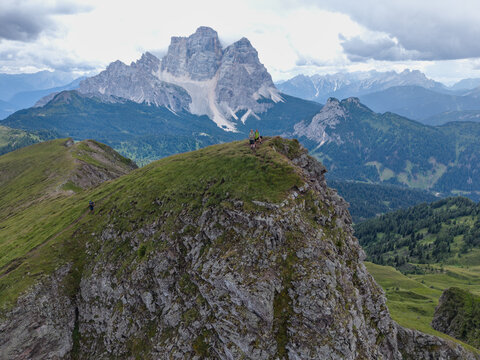 Aerial view of Monte Mondeval and Corvo Alto in the Dolomites with hikers on the rocky ridge, grassy slopes, and dramatic mountain peaks in San Vito di Cadore, Veneto, Italy.