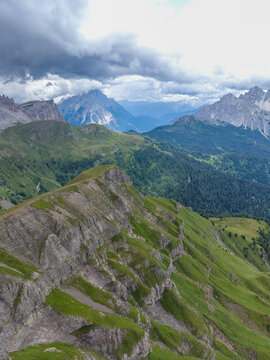 Aerial view of Monte Mondeval Corvo Alto in the Dolomites with lush green slopes, rocky ridges, and a dramatic cloudy sky in San Vito di Cadore, Veneto, Italy.