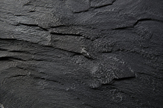 Rough textured dark grey slate stone background with jagged edges and natural uneven surface patterns.