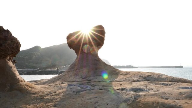 Mushroom shaped hoodoo stone in shiny backlight, against low sun. Bright sunlight beam looks like star when hide behind mushroom top. Characteristic nature-made stone sculpture at Yehliu Geopark