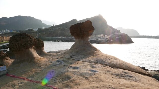 Mushroom rock formation stand at deserted stony shore, bright sun beam, glide shot. Camera move to hide sun disc behind rock cap. Yehliu Geological Park area, focused on details.
