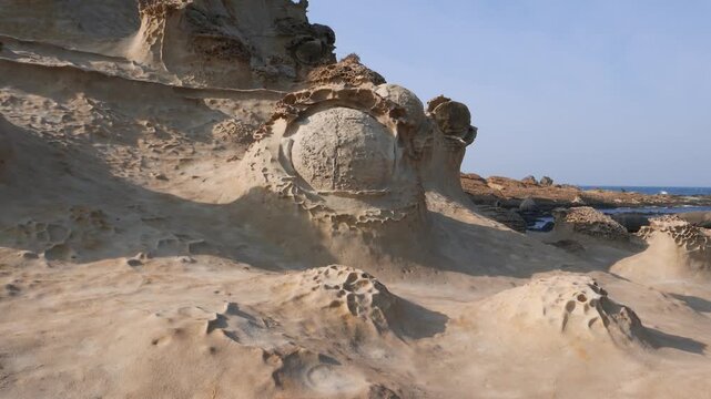Curios stone formations in Yehliu Geopark. Odd shapes of eroded rocks. Camera focus on round stone looks like eye ball, placed against rocky cliff, pan right to sharp sandstone forms