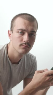 Side view of a young man using a smartphone against a white background, then turning his head to look directly at the camera in a studio shot.