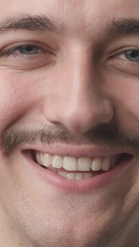 Extreme close-up of a young man's face looking serious at first, then breaking into a warm and joyful smile 