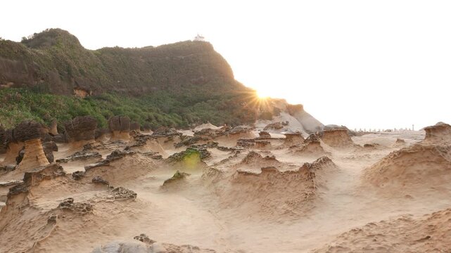 Sunset at stunning Yehliu Geopark landscape, erosion stones formation field. Sun star light over mountain shape on background. Camera move left to sandy futuristic landscape.