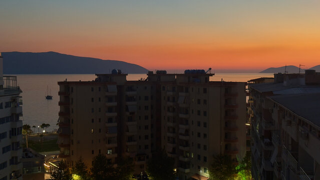 Vibrant orange sunset glow over coastal apartment buildings in Vlore resort city Albania