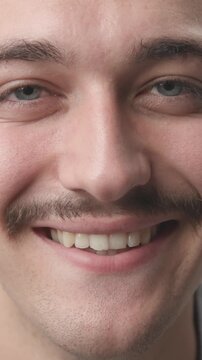Extreme close-up of a young man staring at the camera with a serious face, then breaking into a warm and happy smile 