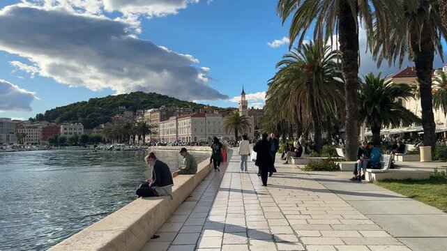 Split, Croatia. People walking through a vibrant plaza lined with palm trees and historic architecture, showcasing a lively atmosphere in a Mediterranean coastal town