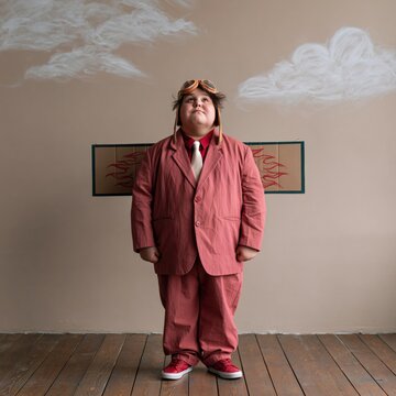 Child in vintage aviator costume with cardboard wings and chalk cloud backdrop for playful portrait background and banner design