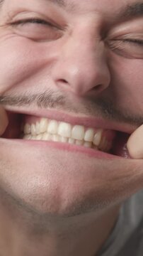 Extreme close-up of a funny young man making silly faces, pulling his cheeks with fingers, showing teeth and tongue 