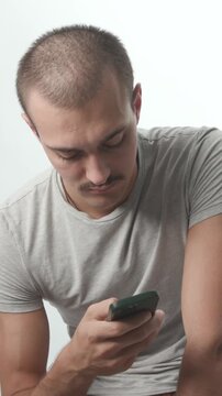 Young man holding a smartphone against a white background, typing and looking up directly at the camera with a calm expression, studio medium shot.