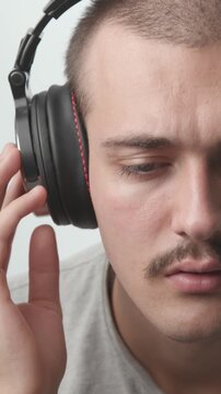 Close-up of a young man wearing headphones, listening to music, then looking up directly at the camera with a gentle smile against a white background.