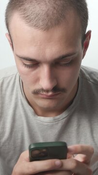 Young man holding a smartphone against a white background, typing and looking up directly at the camera with a calm expression, studio medium shot.