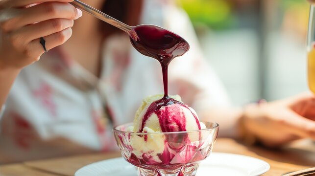 Female hands slowly pouring berry sauce over vanilla ice cream