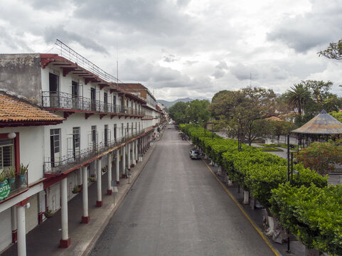 Aerial view of the historic downtown Uruapan featuring colonial architecture with arched porticos and lush green trees lining the street in Uruapan, Michoacan, Mexico.