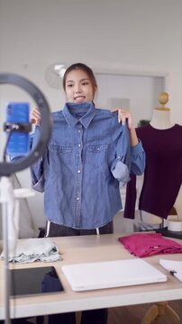 Young Asian fashion influencer presenting denim jacket to camera while filming online clothing review in home studio