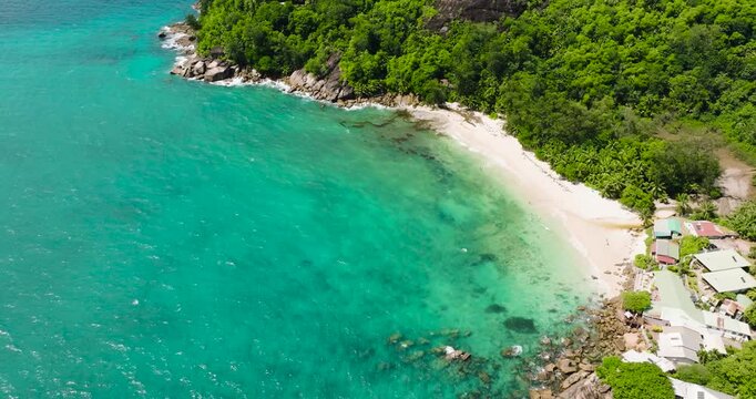 A turquoise lagoon is nestled between green hills and beaches, creating a picturesque scene. Seychelles, Mahe.