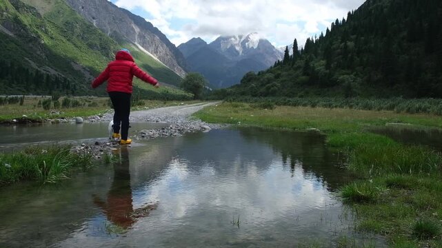 Woman in a red jacket walking with a small dog by a scenic reflection pool in Bayankol Gorge, Kazakhstan. Commercial stock video footage for travel, pet lifestyle, outdoor adventure, and freedom conce